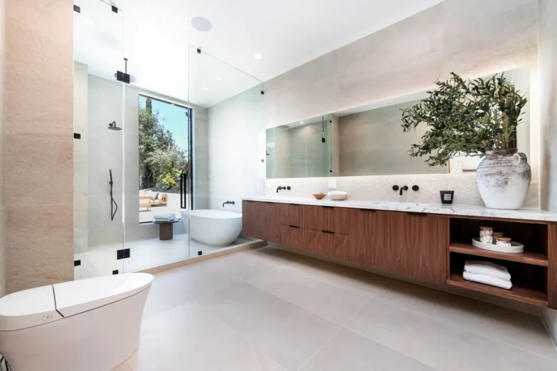 Large bathroom with double vanity, glass shower, freestanding tub and potted tree