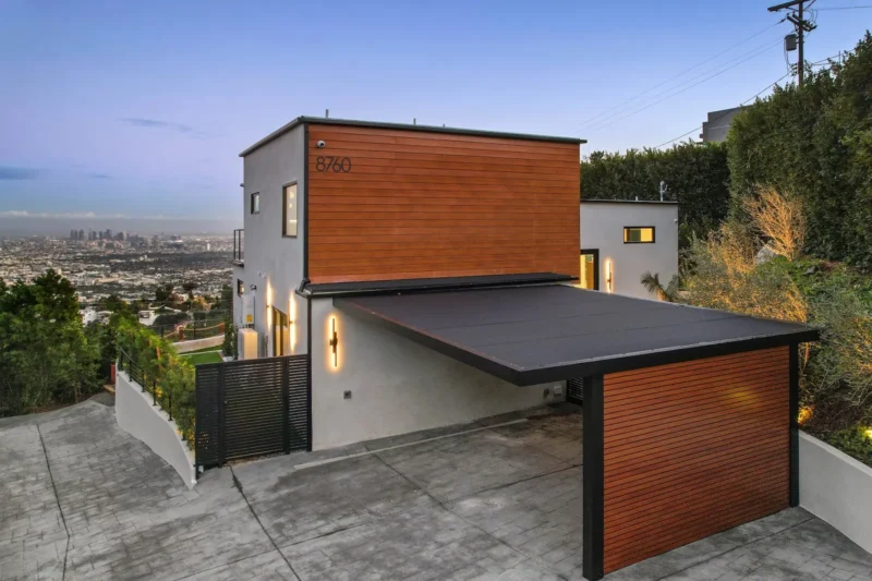 Concrete driveway and carport beside the wood-clad house with city beyond