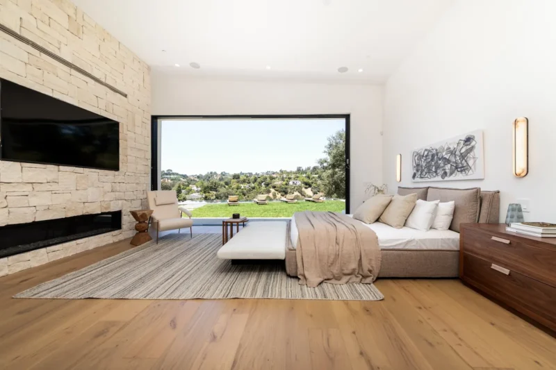 Bedroom with stone fireplace, mounted television and wide window onto garden