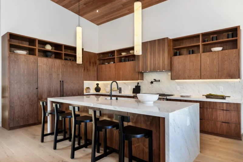 Kitchen with dark wood cabinetry, pale stone island and pendant lights above the seating
