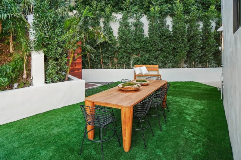 Wood dining table and wire chairs on lawn beside a hedge