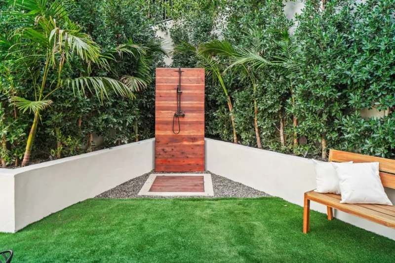 Outdoor shower on a wood panel wall with lawn and bench