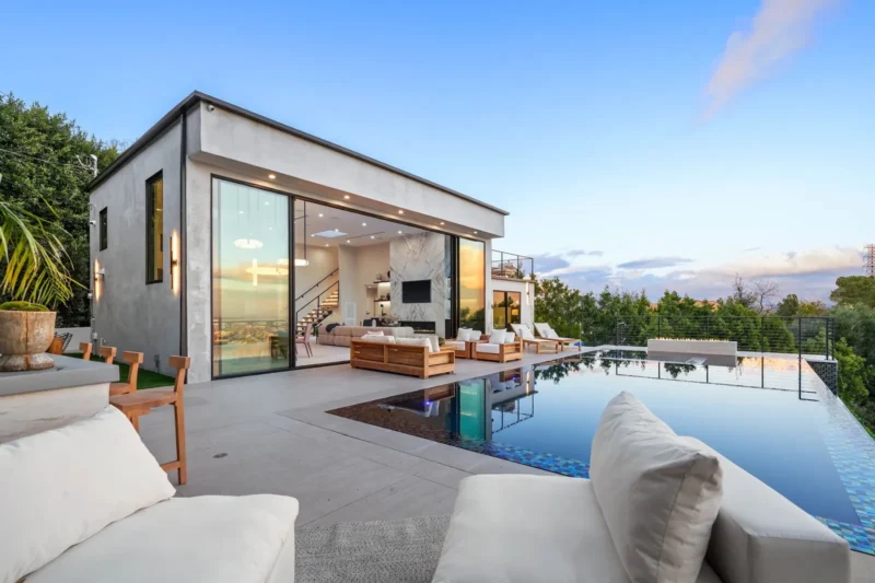 Infinity pool and terrace sofa beside a glass-walled house at dusk